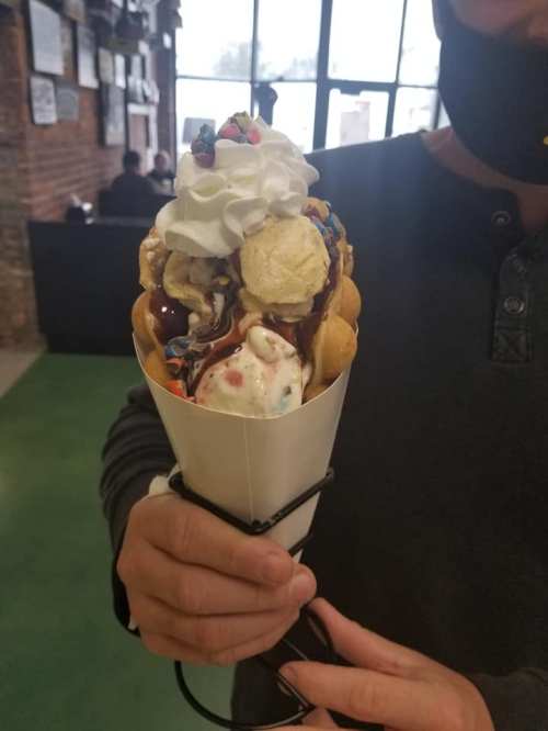 A person holds a large ice cream cone topped with whipped cream, sprinkles, and various flavors of ice cream.