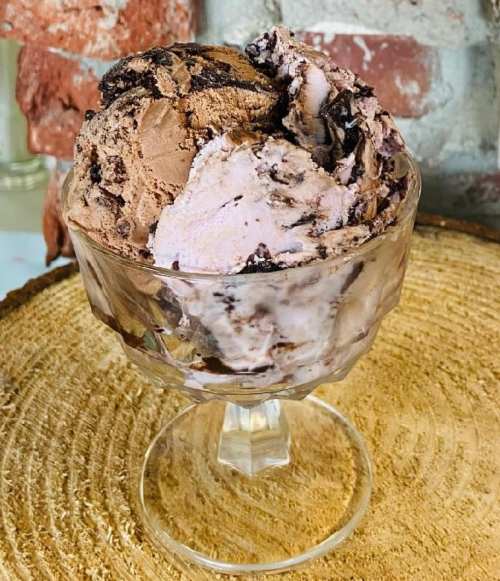 A glass dish filled with scoops of chocolate and berry swirl ice cream on a wooden surface.