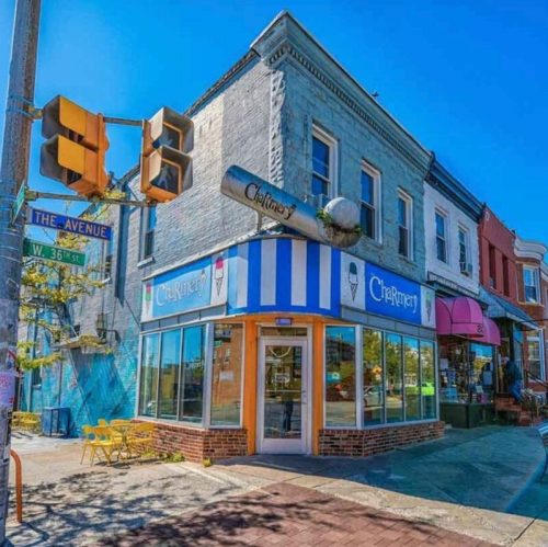 A colorful ice cream shop on a sunny street corner, featuring a striped awning and outdoor seating.