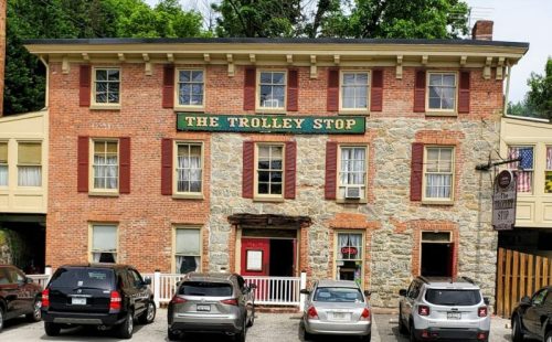 A brick building with a sign reading "The Trolley Stop," featuring several parked cars in front.