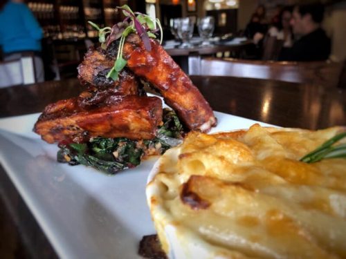 A plate featuring glazed ribs on a bed of greens, alongside a serving of creamy macaroni and cheese.