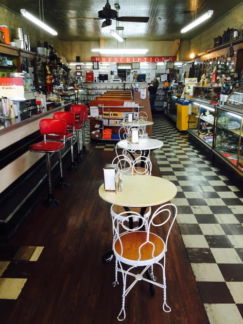 A vintage café interior with red stools, small tables, and a checkered floor, featuring a counter and display cases.