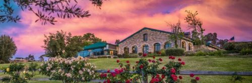 A picturesque building surrounded by blooming roses, set against a vibrant sunset sky.