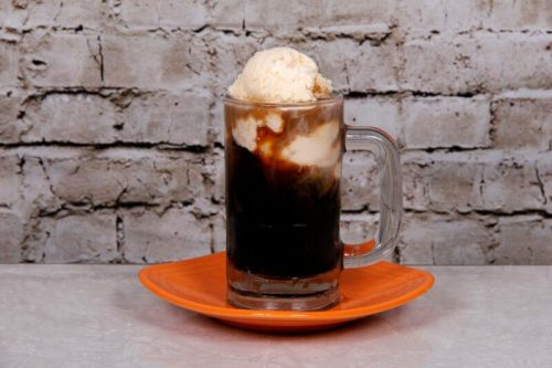 A glass mug filled with root beer and topped with a scoop of vanilla ice cream, served on an orange plate.