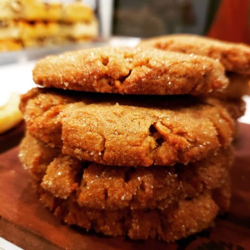 A close-up of a stack of golden-brown cookies, glistening with sugar on a wooden surface.