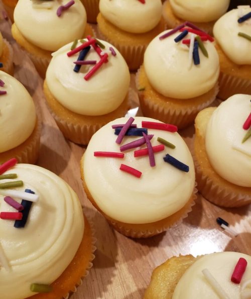 A close-up of yellow cupcakes topped with creamy frosting and colorful sprinkles on a wooden surface.