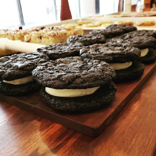 A close-up of dark chocolate cookies with a creamy filling, arranged on a wooden platter.