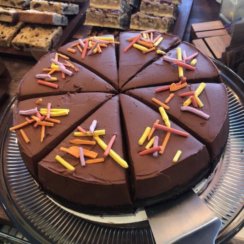 A round chocolate cake sliced into eight pieces, topped with colorful sprinkles on a glass platter.