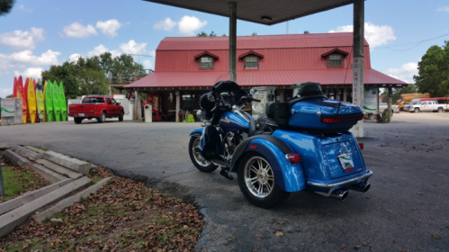 A blue motorcycle with a sidecar parked in front of a rustic building and colorful kayaks in the background.