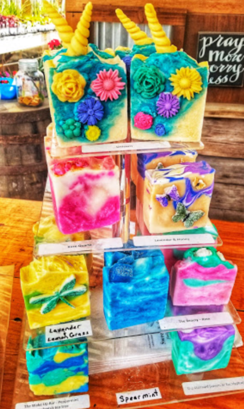 Colorful handmade soaps in various shapes and designs, displayed on a wooden table with floral decorations.