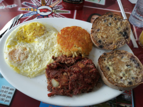 A plate of breakfast featuring two eggs, hash browns, corned beef hash, and toasted blueberry muffins.