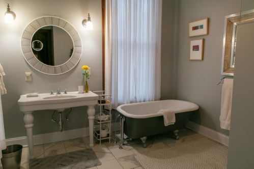 A stylish bathroom featuring a vintage tub, a round mirror, and a small flower vase on a sink. Soft lighting and decor.