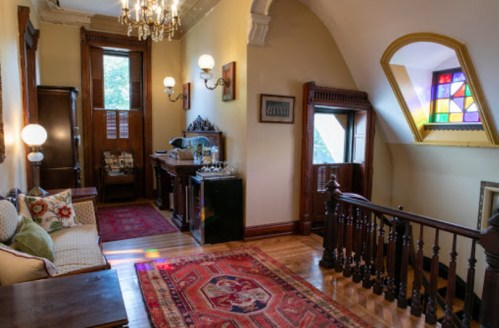 A cozy hallway with a vintage sofa, wooden railings, and a colorful stained glass window.
