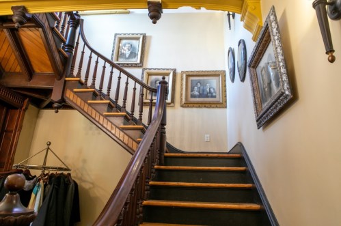 A wooden staircase leads to an upper floor, adorned with vintage framed portraits on the wall.
