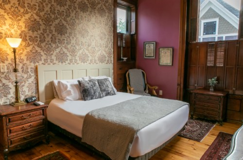 Cozy bedroom with a queen bed, vintage decor, and warm lighting, featuring floral wallpaper and wooden furniture.
