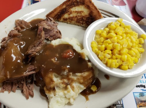 A plate with shredded beef in gravy, mashed potatoes, corn, and a slice of toasted bread.