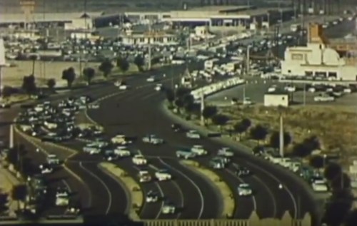 Aerial view of a busy highway with numerous cars and a commercial area in the background.