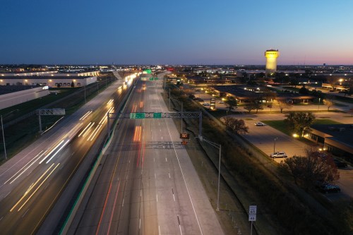 Aerial view of a highway at dusk, with light trails from vehicles and a water tower in the background.