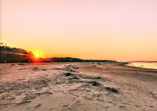 Sunset over a serene beach, with gentle waves and silhouettes of people walking along the shore.