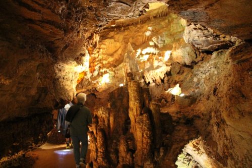 A person walks through a dimly lit cave, surrounded by rock formations and illuminated stalactites.