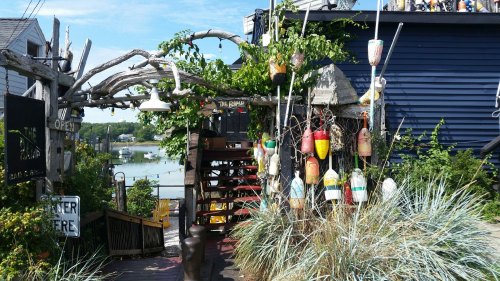 A colorful entrance with buoy decorations leads to a waterfront building surrounded by greenery and a clear blue sky.