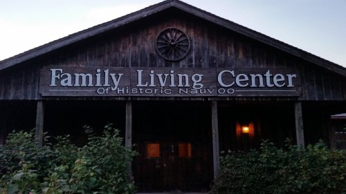 Sign for the Family Living Center of Historic Nauvoo, featuring a wooden building with a wheel decoration.