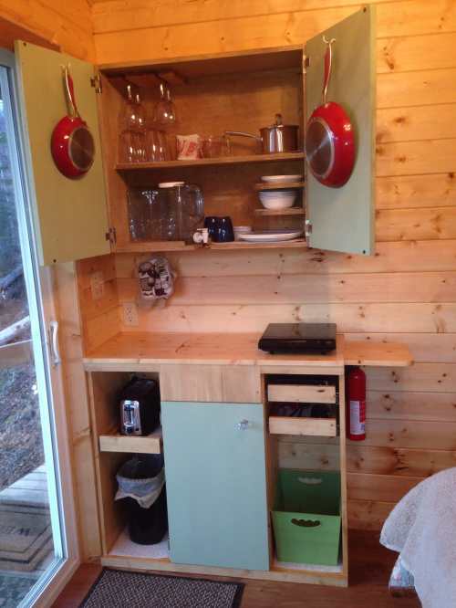 A cozy wooden kitchen corner with green cabinets, shelves of dishes, and a small countertop with appliances.