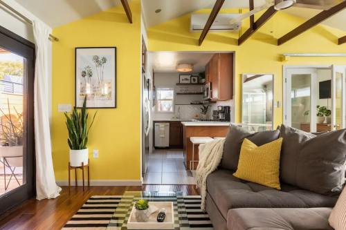 Cozy living space with yellow walls, a gray sofa, and a view of a kitchen, featuring plants and modern decor.