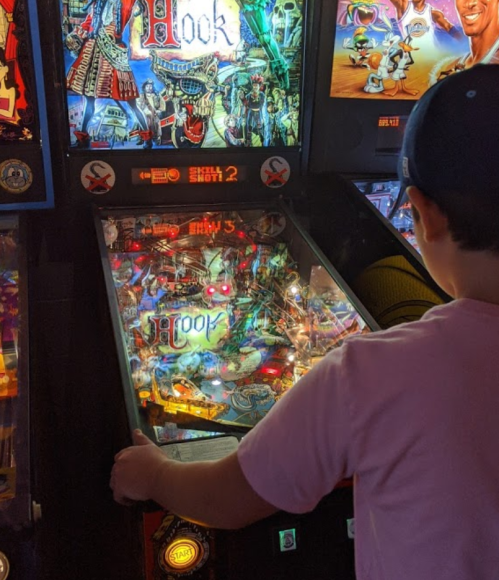 A child plays a colorful pinball machine titled "Hook" in an arcade, focused on the game.