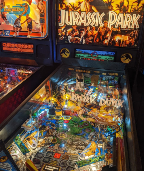 A close-up of a Jurassic Park pinball machine, featuring vibrant artwork and a detailed playfield with dinosaur themes.