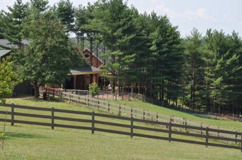 A scenic view of a farmhouse surrounded by trees and a wooden fence on a sunny day.