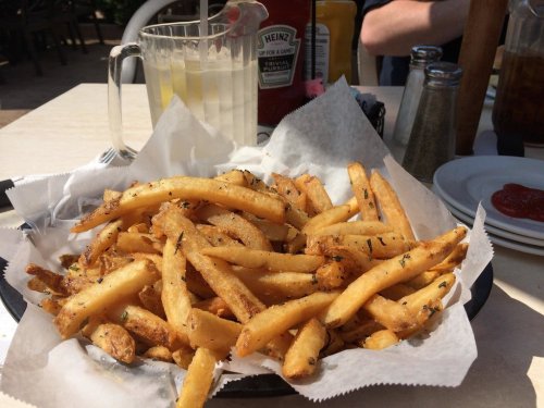 A basket of golden, crispy French fries garnished with herbs, served with condiments in a casual dining setting.
