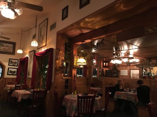 Cozy restaurant interior with wooden decor, dim lighting, and tables set for dining. Two patrons are seated at separate tables.