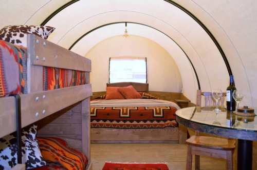 Cozy interior of a glamping tent featuring a bunk bed, a double bed, and a dining table with wine glasses.