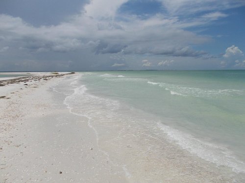 A serene beach with soft waves lapping at the shore, under a partly cloudy sky.
