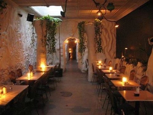 Cozy restaurant interior with textured walls, soft lighting, and tables lined along a narrow corridor.