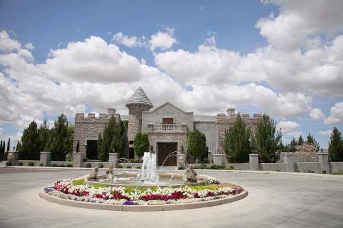 A grand stone castle with a fountain and colorful flower beds, set against a blue sky with fluffy clouds.