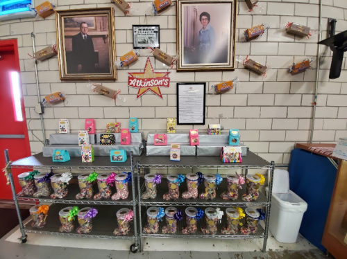 A display of colorful candy jars and gift boxes on shelves, with framed portraits on the wall behind.