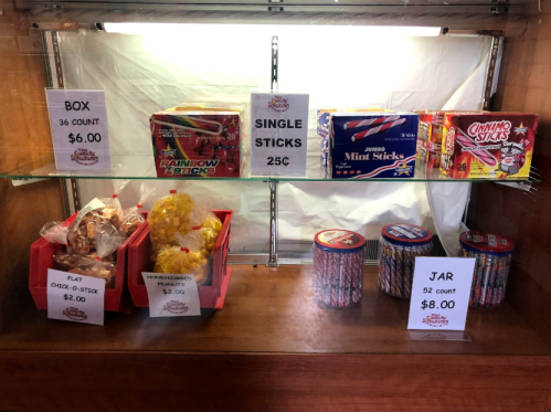 Display case with various candy sticks: boxes, single sticks, and jars, with prices listed.