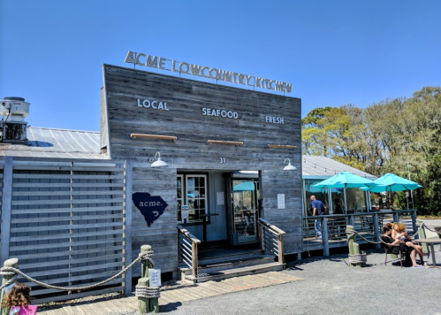 Exterior of Acme Lowcountry Kitchen, featuring a wooden facade, outdoor seating, and a clear blue sky.