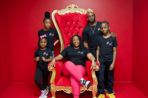 A family poses together in matching black shirts in front of a red wall, seated on a large ornate throne.