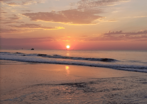 A serene beach at sunset, with vibrant orange and pink hues reflecting on the water and gentle waves lapping at the shore.