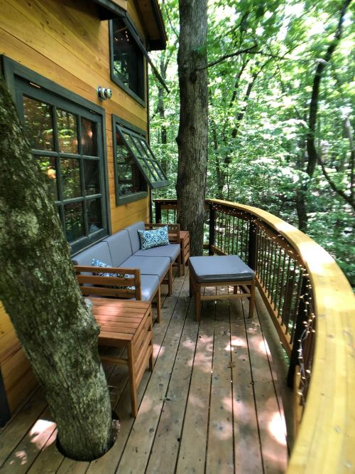Cozy wooden deck with seating, surrounded by trees in a lush forest setting.