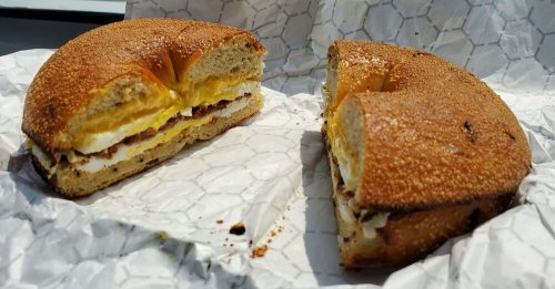 A toasted bagel sandwich cut in half, filled with eggs and bacon, resting on crumpled paper.