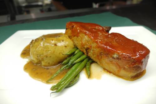 A plate featuring meatloaf with tomato glaze, green beans, and mashed potatoes with gravy.