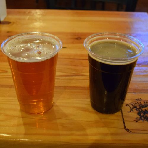 Two plastic cups of beer on a wooden table: one amber and one dark brown.