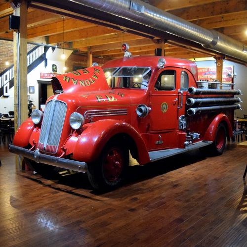 A vintage red fire truck displayed indoors, featuring chrome details and hoses, set in a rustic restaurant environment.