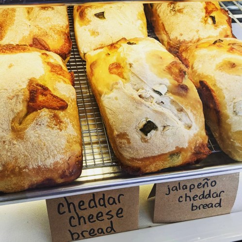 Freshly baked loaves of cheddar cheese bread and jalapeño cheddar bread on a display rack.