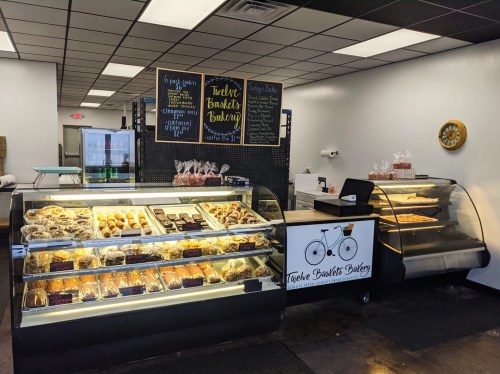 A bakery display with various pastries and desserts, featuring a chalkboard menu and a bicycle-themed counter.