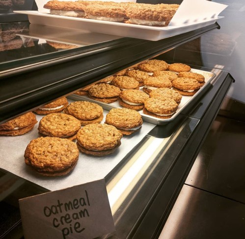 A display case filled with oatmeal cream pies on a tray, with a sign labeling them.